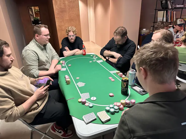 Det grønne bordet. Chips i potten, en spiller sjekker mobilen.